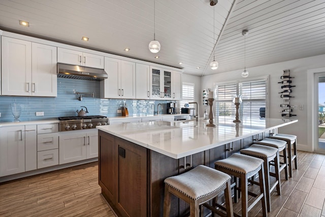 kitchen featuring lofted ceiling, under cabinet range hood, stainless steel gas cooktop, white cabinets, and backsplash