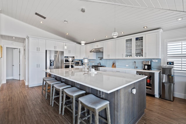 kitchen featuring under cabinet range hood, high end refrigerator, visible vents, and decorative backsplash