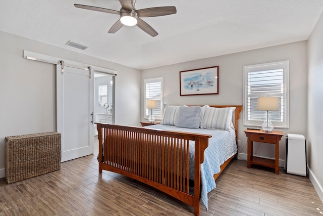 bedroom with a barn door, baseboards, light wood-style flooring, ensuite bathroom, and a textured ceiling