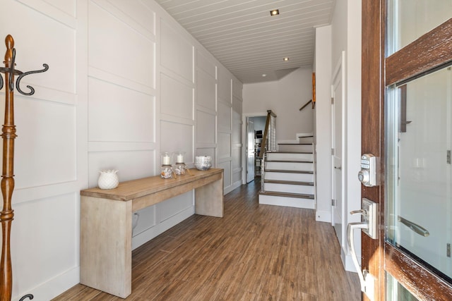 entryway featuring dark wood finished floors, a decorative wall, and stairs