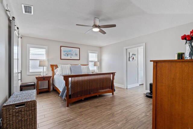 bedroom featuring a barn door, multiple windows, visible vents, and wood finished floors