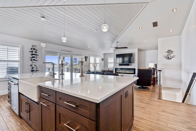 kitchen featuring decorative light fixtures, a fireplace, lofted ceiling, light wood-style floors, and a sink