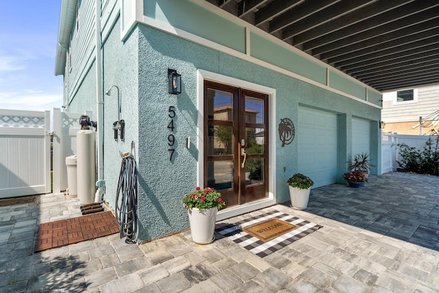 doorway to property with fence, decorative driveway, and stucco siding