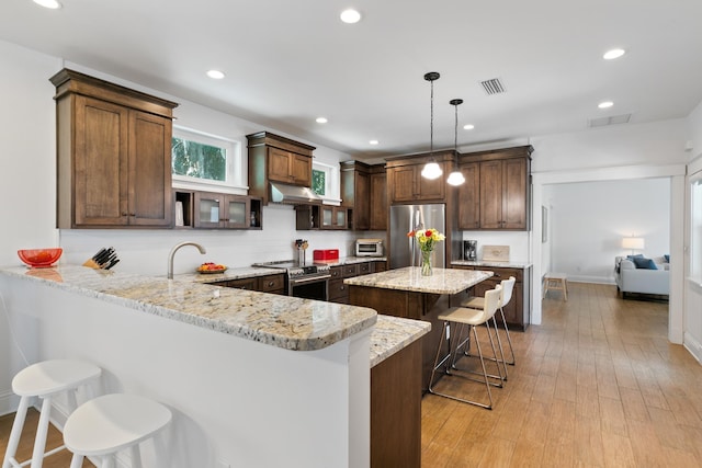 kitchen featuring stainless steel appliances, a peninsula, hanging light fixtures, light stone countertops, and a kitchen bar