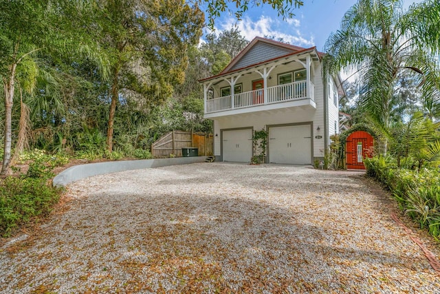 view of front facade with an attached garage, a balcony, a gate, and gravel driveway