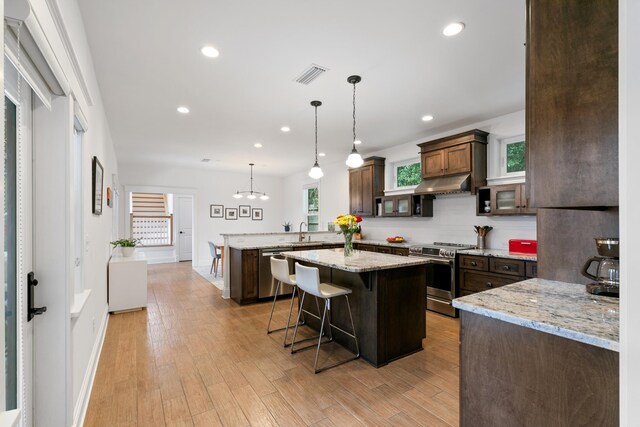 kitchen featuring glass insert cabinets, a sink, a kitchen breakfast bar, appliances with stainless steel finishes, and decorative light fixtures