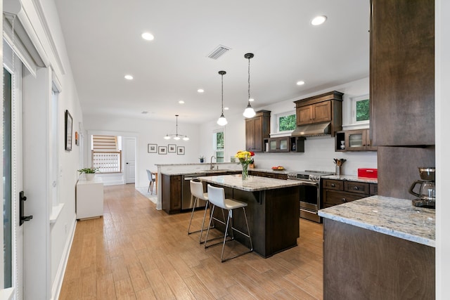 kitchen featuring visible vents, appliances with stainless steel finishes, a breakfast bar, a peninsula, and under cabinet range hood