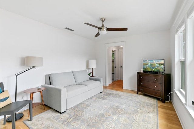 living room with light wood-style flooring, visible vents, and ceiling fan