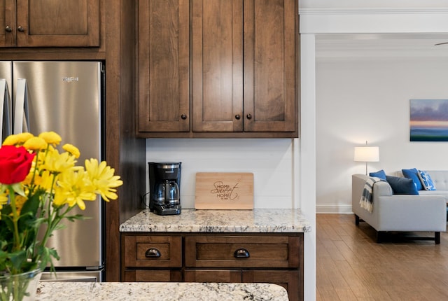 kitchen with dark brown cabinetry, light wood-type flooring, freestanding refrigerator, and light stone countertops