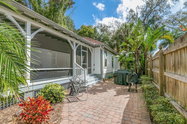 view of patio featuring a sunroom, a fenced backyard, and a grill