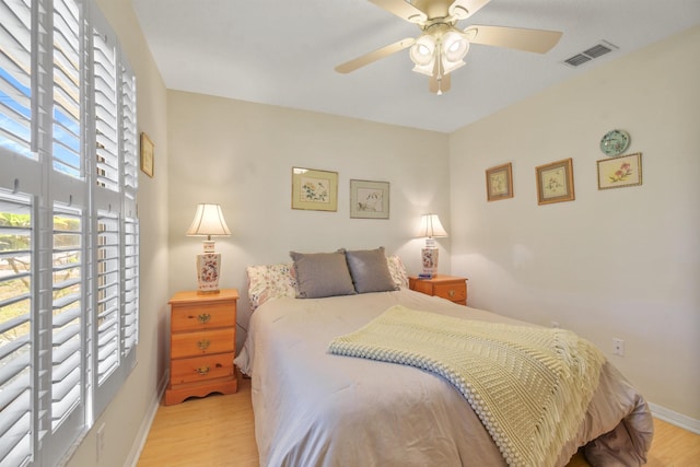 bedroom with a ceiling fan, visible vents, baseboards, and wood finished floors