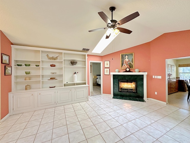 unfurnished living room with light tile patterned floors, ceiling fan, visible vents, lofted ceiling with skylight, and a tiled fireplace