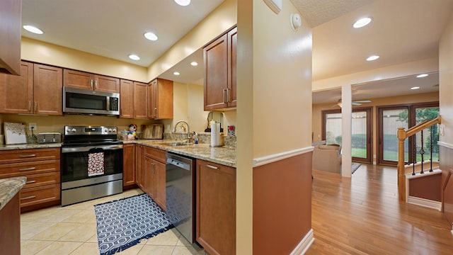 kitchen with light stone counters, stainless steel appliances, ceiling fan, sink, and light hardwood / wood-style flooring