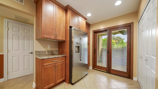 kitchen with stainless steel fridge, light tile patterned flooring, and light stone counters