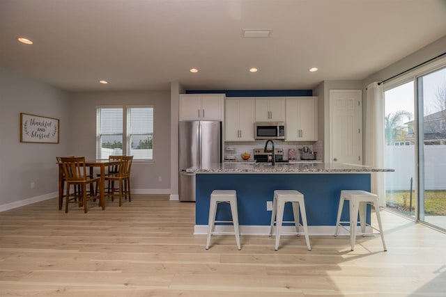 kitchen featuring tasteful backsplash, appliances with stainless steel finishes, a healthy amount of sunlight, white cabinetry, and an island with sink