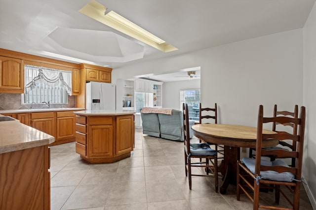 kitchen with light tile patterned floors, ceiling fan, a tray ceiling, white refrigerator with ice dispenser, and a kitchen island