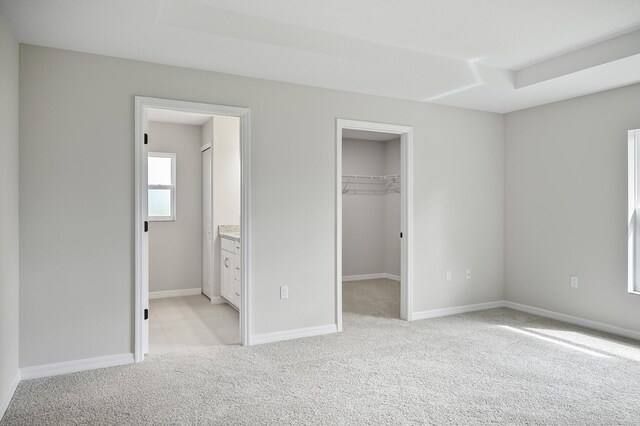 unfurnished bedroom with light colored carpet, ensuite bathroom, a closet, and a walk in closet