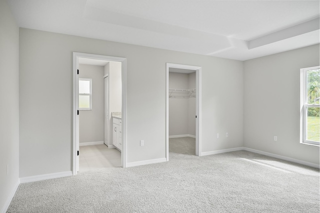 unfurnished bedroom with a spacious closet, multiple windows, light carpet, and ensuite bath