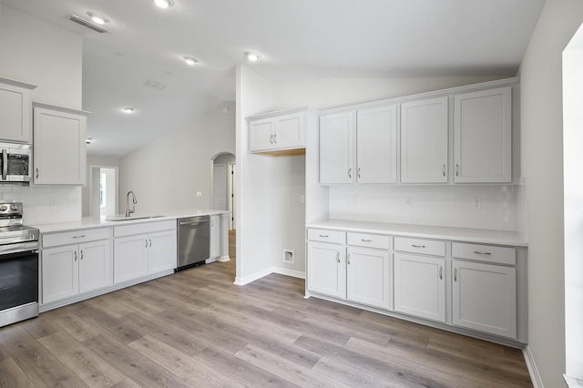 kitchen with light wood-type flooring, appliances with stainless steel finishes, lofted ceiling, and sink