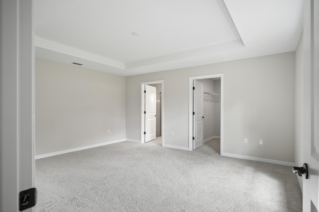 unfurnished bedroom featuring a spacious closet, connected bathroom, a closet, and a raised ceiling