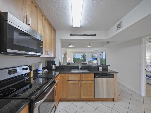 kitchen with sink, dark stone countertops, a textured ceiling, light tile patterned floors, and appliances with stainless steel finishes