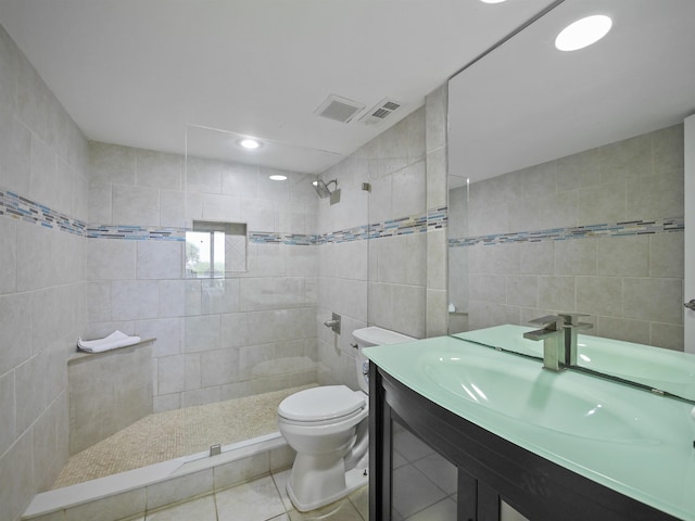 bathroom with tile patterned flooring, tiled shower, toilet, vanity, and tile walls