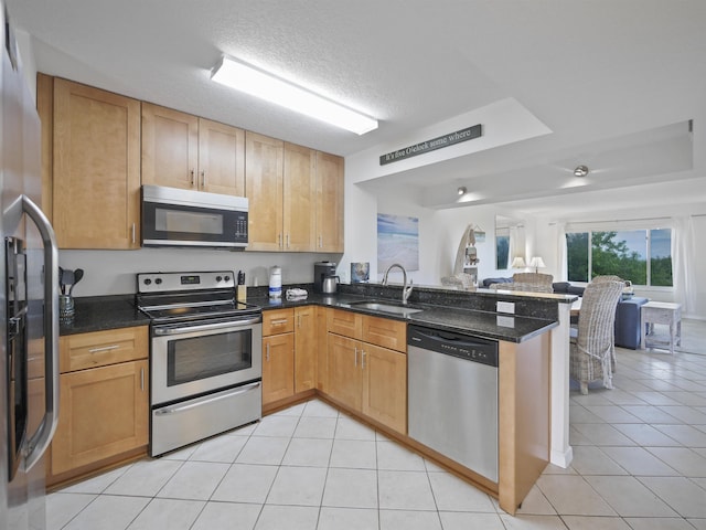 kitchen featuring sink, kitchen peninsula, stainless steel appliances, and dark stone counters