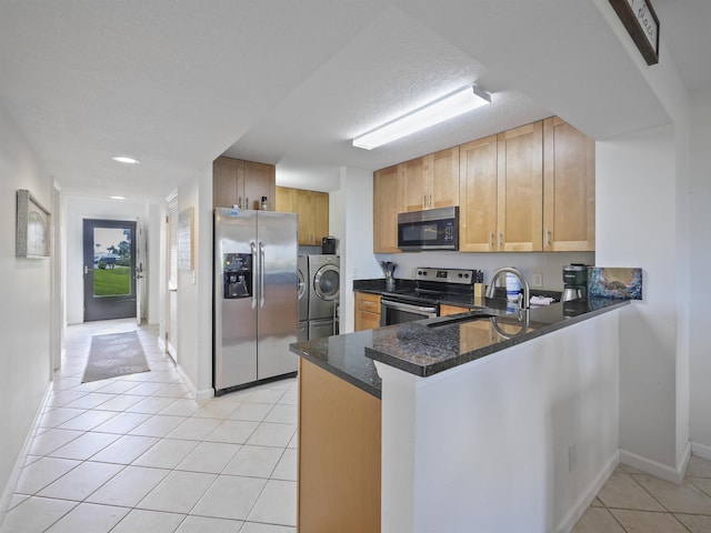 kitchen with dark stone countertops, light tile patterned flooring, washer / dryer, kitchen peninsula, and stainless steel appliances