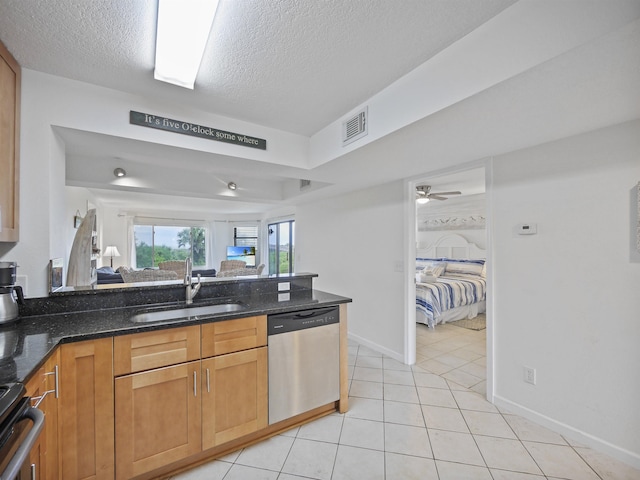 kitchen with sink, dark stone counters, a textured ceiling, light tile patterned floors, and appliances with stainless steel finishes