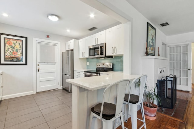 kitchen featuring backsplash, white cabinets, appliances with stainless steel finishes, kitchen peninsula, and a breakfast bar area