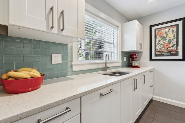 kitchen with backsplash, light stone counters, white cabinetry, and sink