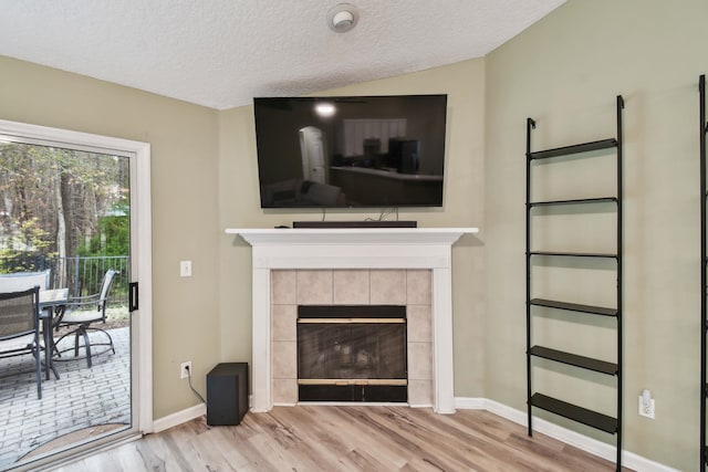 living room featuring a textured ceiling, a tiled fireplace, wood finished floors, and baseboards