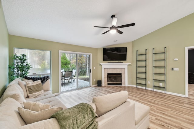 living room with a textured ceiling, a fireplace, light hardwood / wood-style flooring, ceiling fan, and lofted ceiling