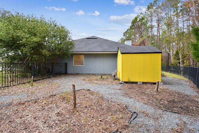 back of property featuring an outbuilding, a fenced backyard, roof with shingles, a shed, and a chimney