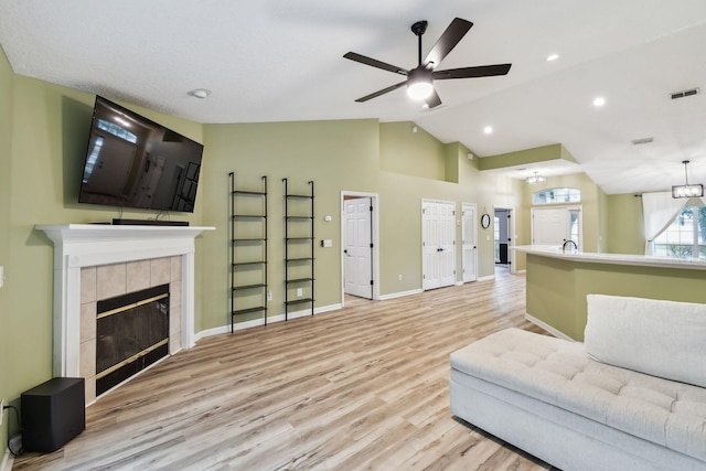 living room with light wood finished floors, baseboards, visible vents, a tile fireplace, and vaulted ceiling