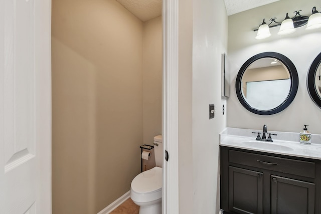 bathroom with baseboards, vanity, toilet, and a textured ceiling