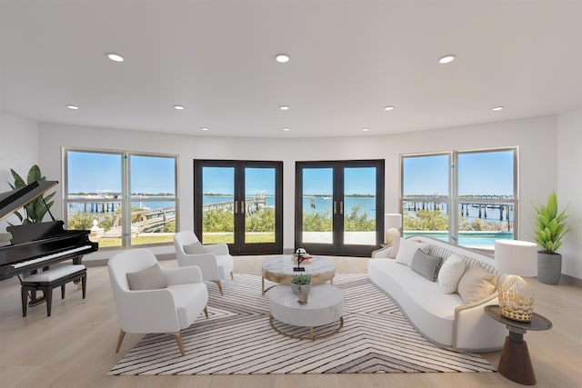 living room featuring a wealth of natural light, french doors, a water view, and light hardwood / wood-style floors