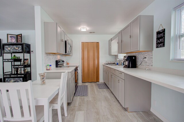 kitchen featuring appliances with stainless steel finishes, backsplash, gray cabinetry, sink, and light hardwood / wood-style flooring