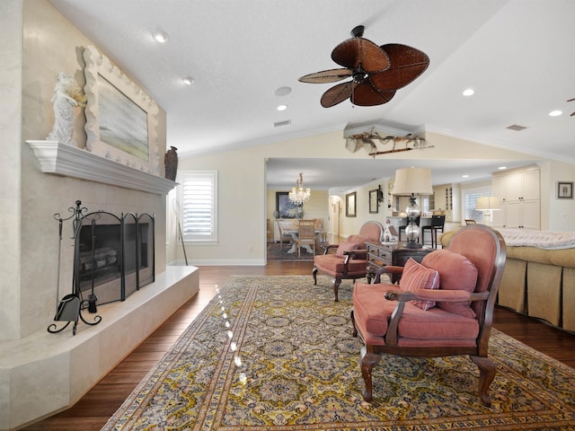 living room with ceiling fan with notable chandelier, vaulted ceiling, hardwood / wood-style flooring, ornamental molding, and a fireplace