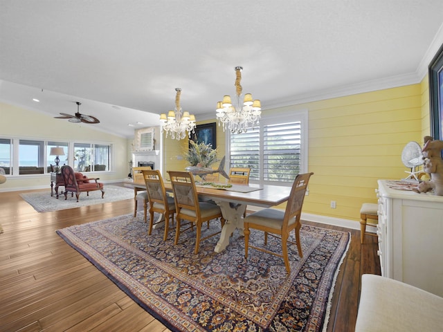 dining space with ceiling fan with notable chandelier, wood-type flooring, lofted ceiling, and crown molding