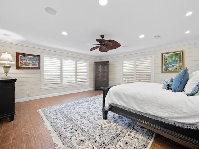 bedroom with ceiling fan, wooden walls, ornamental molding, and hardwood / wood-style flooring