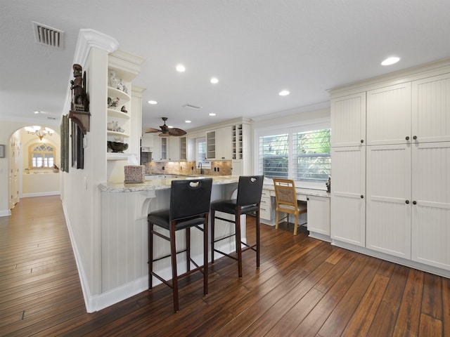 kitchen featuring ceiling fan, white cabinetry, a kitchen breakfast bar, dark hardwood / wood-style flooring, and ornamental molding