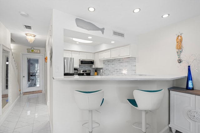 kitchen featuring a breakfast bar, appliances with stainless steel finishes, kitchen peninsula, and white cabinetry