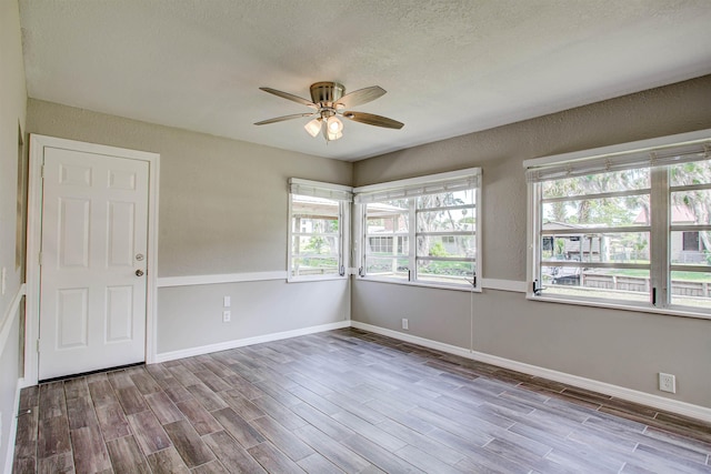 empty room with baseboards, a ceiling fan, wood finished floors, and a textured ceiling