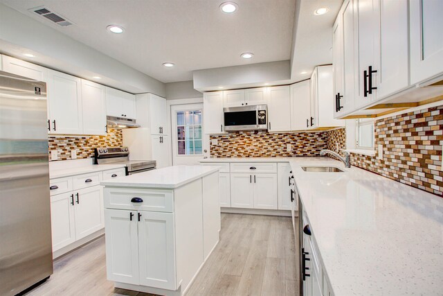 kitchen with under cabinet range hood, stainless steel appliances, visible vents, a sink, and light wood-type flooring