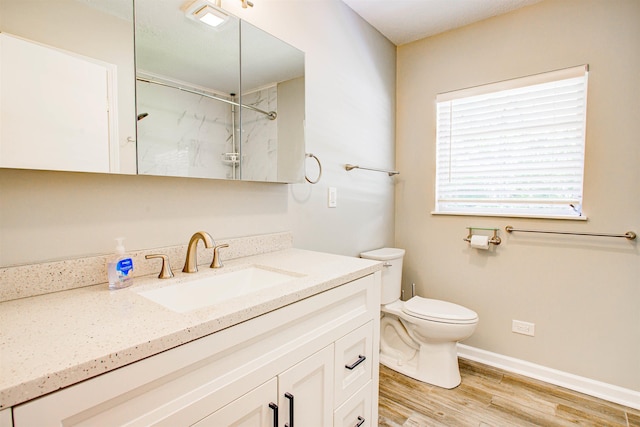 bathroom featuring a marble finish shower, toilet, baseboards, wood finished floors, and vanity