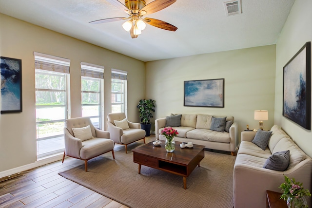 living area featuring wood finished floors, visible vents, baseboards, and ceiling fan