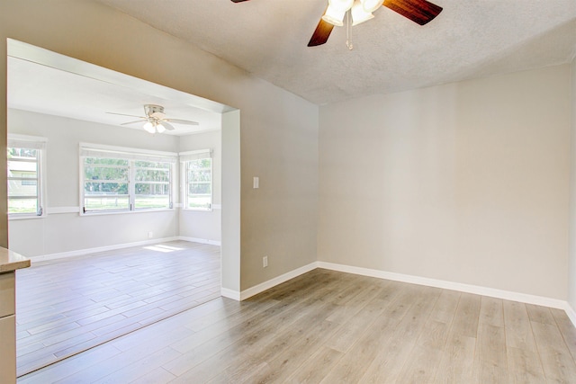 spare room featuring light wood finished floors, a ceiling fan, and baseboards