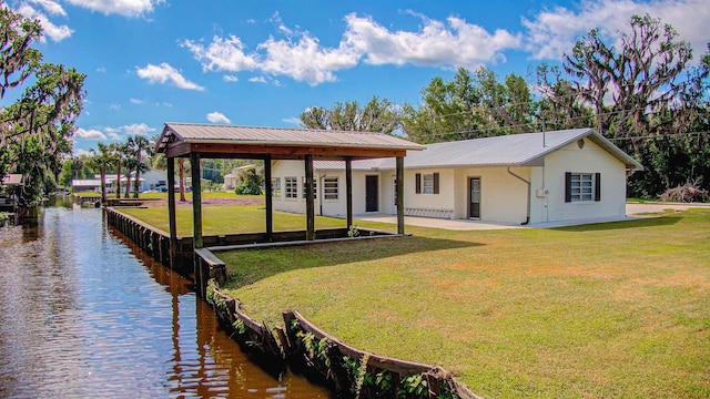 back of house with stucco siding, a lawn, a water view, and metal roof