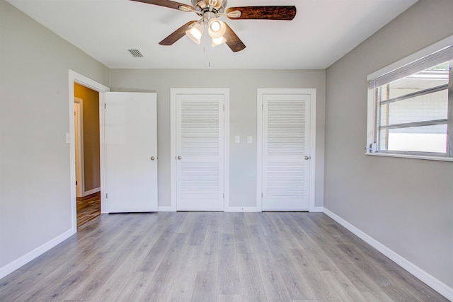 unfurnished bedroom featuring light wood finished floors, baseboards, multiple closets, and visible vents